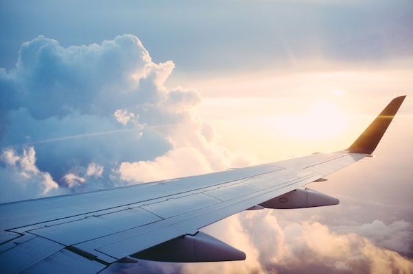 look on a wing of a flying plane above the clouds with the rising sun in the background